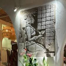 A stone relief of a Mayan-like figure holding a flower next to a grid of symbols.