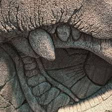 A close-up of a stone sculpture showing a creature's mouth with large fangs.